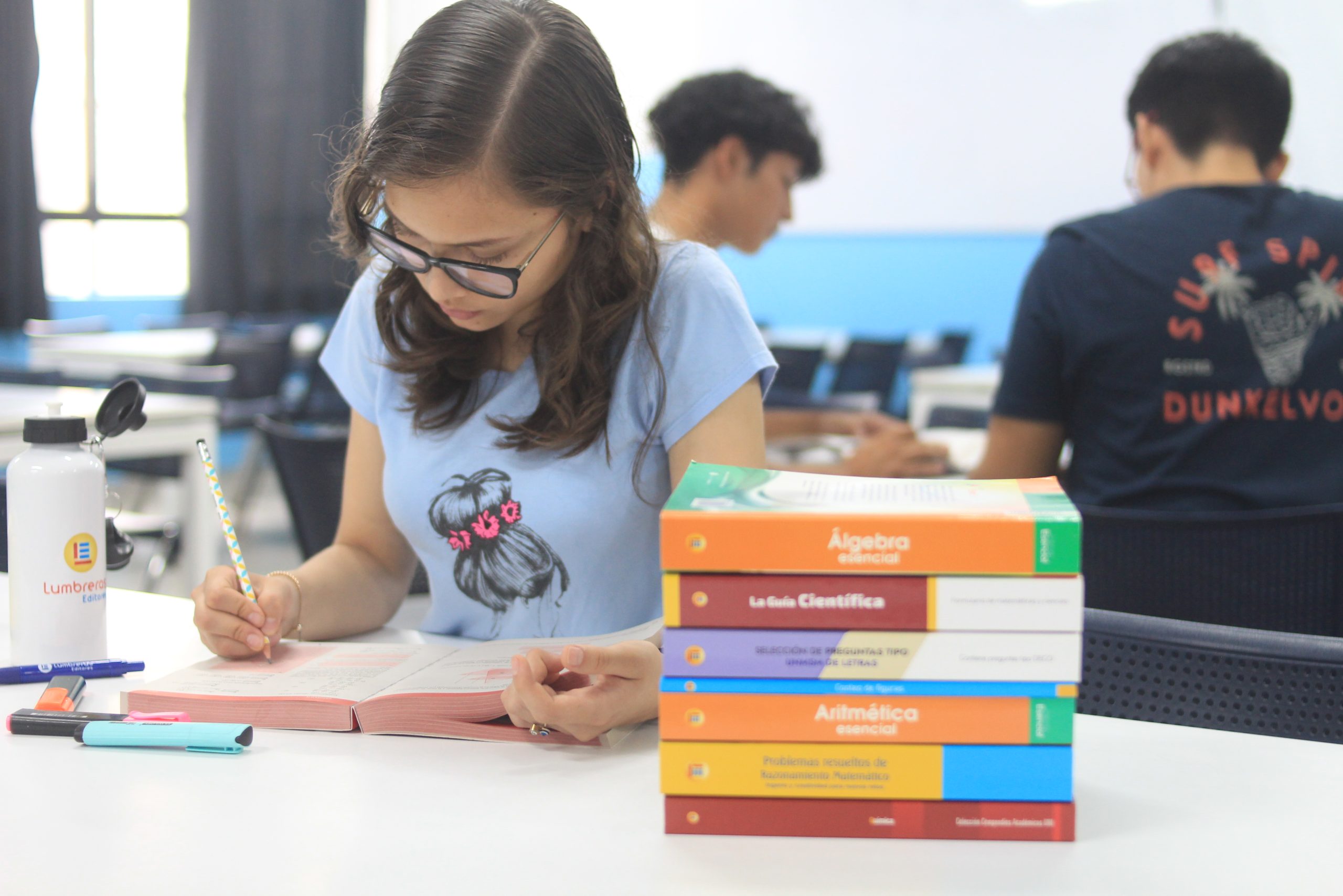 Estudiante en biblioteca con libros preuniversitarios de Lumbreras Editores